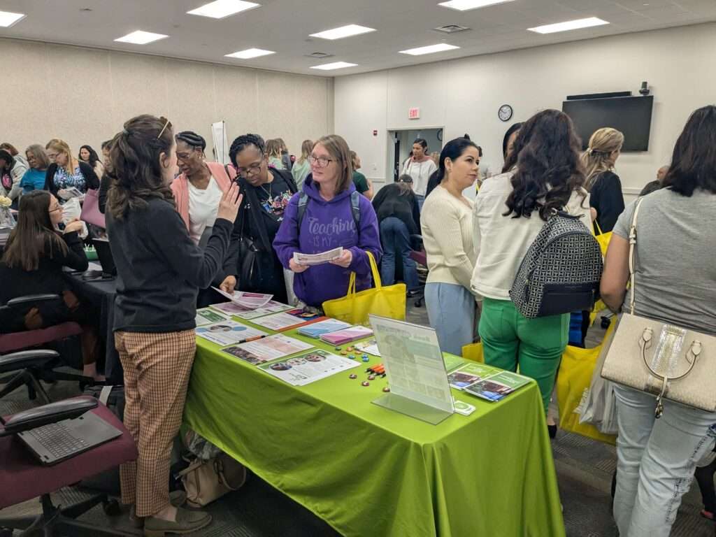 Library outreach specialist talks with childcare providers across a library information table.